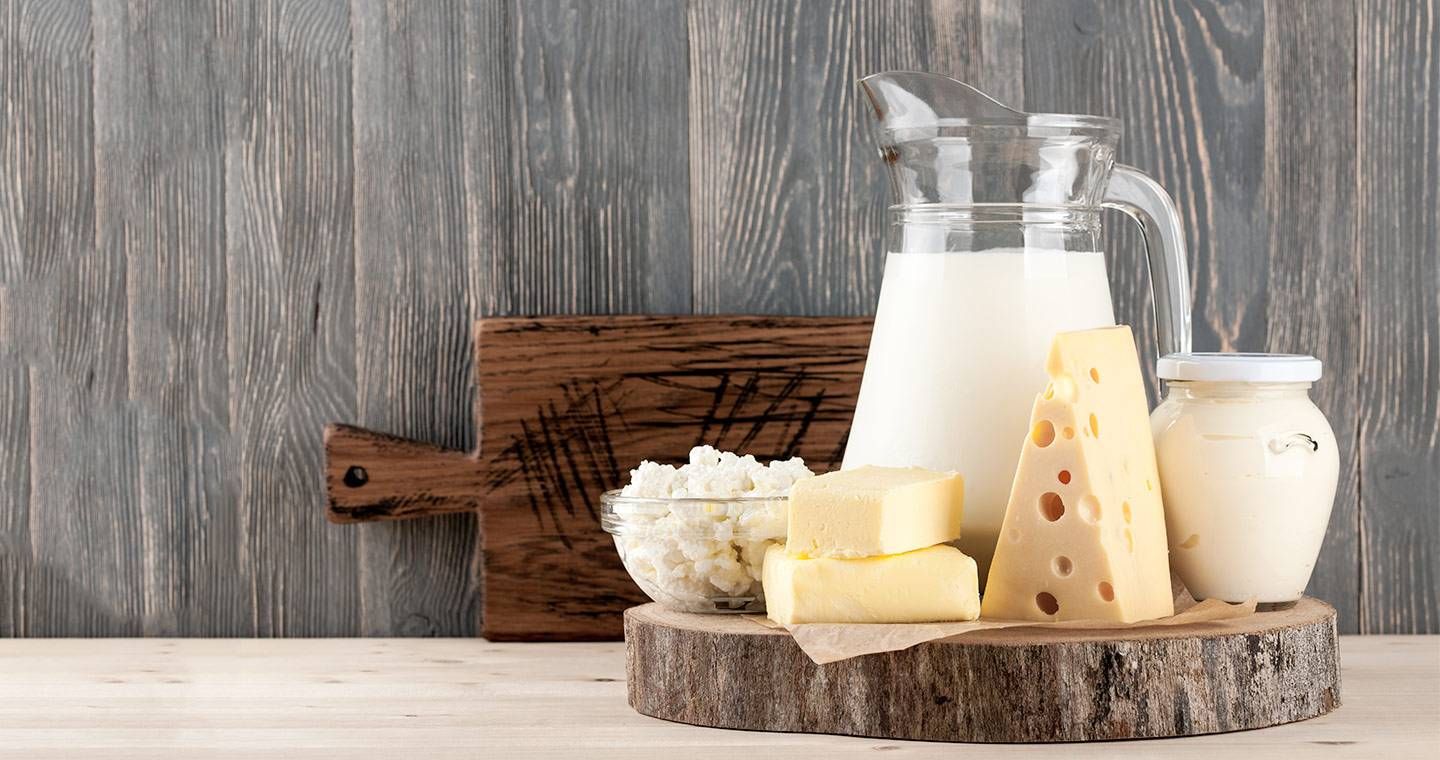 Caraffa di latte con burro, ricotta e formaggio a fette su tavolo in legno