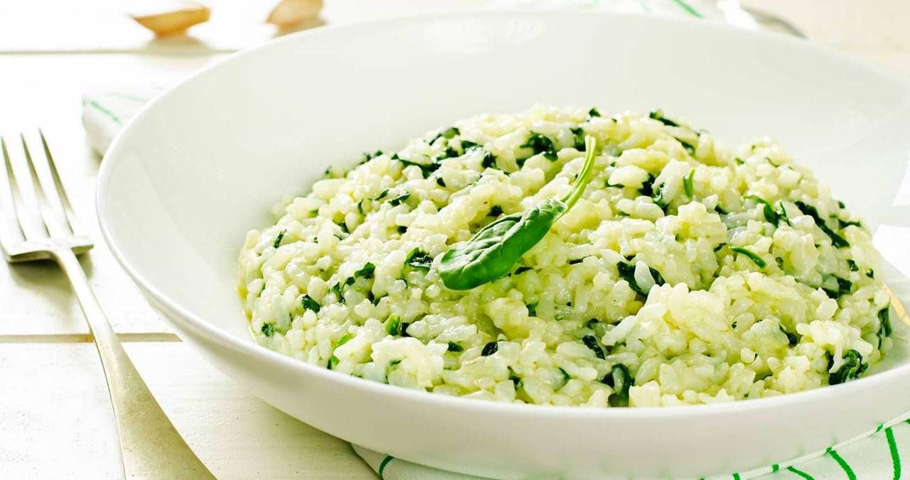 Risotto cremoso agli spinaci servito in un piatto bianco con foglia di spinacio fresca